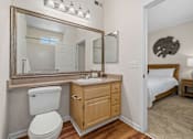 Thumbnail 23 of 30 - A bathroom with a toilet, sink, mirror, and a bed in the background.