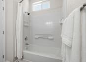 Thumbnail 24 of 30 - A white bathroom with a tub, towel, and shower curtain.
