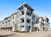 Thumbnail 24 of 32 - A large, modern apartment complex with multiple balconies and a clear blue sky above.