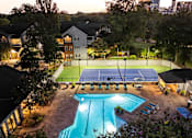 Thumbnail 28 of 29 - A tennis court is lit up at night with a pool in the foreground.