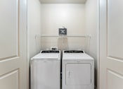 Thumbnail 28 of 32 - Two white front loading washing machines in a laundry room.