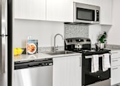 Thumbnail 6 of 29 - A modern kitchen with a black stove top oven and white cabinets.