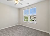 Thumbnail 38 of 45 - A room with a ceiling fan and a window overlooking a building.