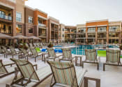 Thumbnail 5 of 75 - Rows of chaise lounge chairs around an outdoor pool surrounded by apartment buildings at The Apex at CityPlace, Kansas, 66210