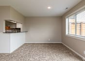 Thumbnail 4 of 19 - A spacious room with a window and a kitchen area in the background.
