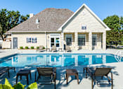 Thumbnail 3 of 44 - A poolside lounge area with chairs and tables is in front of a house.