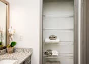 Thumbnail 37 of 50 - A bathroom with a large mirror, a sink, and a shelf with towels and toiletries.
