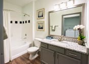 Thumbnail 6 of 50 - A bathroom with a white toilet, a bathtub with a shower curtain, a sink with a mirror, and a potted plant.