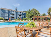 Thumbnail 7 of 34 - A poolside table with chairs and a building in the background.