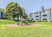 Thumbnail 19 of 34 - A playground with a slide and a green tree in front of a building.