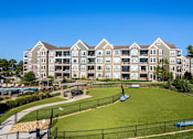 Thumbnail 18 of 53 - an exterior view of an apartment building with a green field and a tennis court  at Waterside Residences on Quivira, Lenexa, Kansas