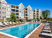 Thumbnail 16 of 53 - a swimming pool with lounge chairs in front of an apartment building  at Waterside Residences on Quivira, Lenexa, Kansas