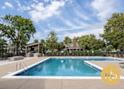 Thumbnail 10 of 28 - A large outdoor swimming pool surrounded by trees and a covered area.