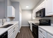 Thumbnail 4 of 28 - A kitchen with white cabinets and black appliances.