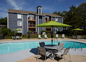 Thumbnail 9 of 34 - A pool with chairs and umbrellas in front of a grey building.