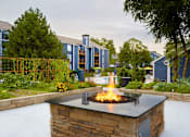 Thumbnail 2 of 34 - A fire pit in the middle of a garden with a building in the background.