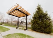 Thumbnail 13 of 23 - a pergola in a park with a tree and a bench