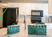 Thumbnail 3 of 25 - A black refrigerator and microwave in a kitchen with white cabinets.