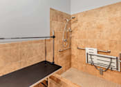 Thumbnail 24 of 50 - A tiled shower area with a bench and a handheld shower head.