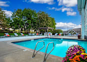Thumbnail 13 of 25 - A pool with a diving board and chairs around it.