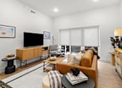 Thumbnail 4 of 12 - A living room with a brown sofa, a black table, and a TV.