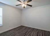 Thumbnail 8 of 15 - A room with a ceiling fan and wooden flooring.