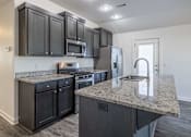 Thumbnail 1 of 15 - A kitchen with black cabinets and granite countertops.