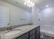 Thumbnail 12 of 15 - A bathroom with a marble countertop and a white tub.