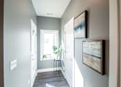 Thumbnail 14 of 18 - A hallway with a table and two framed pictures on the wall.