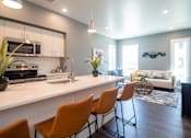 Thumbnail 3 of 18 - A modern kitchen with white countertops and orange chairs.