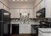 Thumbnail 17 of 23 - A black refrigerator is on the left in a kitchen with white cabinets.