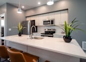 Thumbnail 4 of 18 - A modern kitchen with a white countertop and orange chairs.