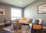 Thumbnail 3 of 18 - A living room with a grey couch, a yellow throw, and a woven chair.