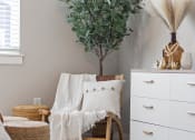 Thumbnail 27 of 36 - a living room with a chair and a white dresser and a plant at Hillcrest Village, Arkansas