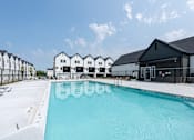 Thumbnail 14 of 18 - A swimming pool in front of a building with a clear blue sky.