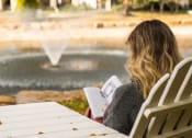 Thumbnail 48 of 50 - a woman sitting in a chair reading a book in front of a fountain