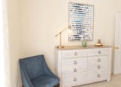 Thumbnail 34 of 44 - A blue chair sits in front of a white dresser with a framed artwork on the wall. at The Crest at Sugarloaf, Lawrenceville, Georgia