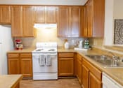 Thumbnail 14 of 44 - A kitchen with wooden cabinets and a white stove top oven. at The Crest at Sugarloaf, Lawrenceville