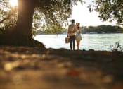 Thumbnail 61 of 66 - a man and a woman standing under a tree by the water at District at Riverside Apartments, Chattanooga