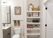 Thumbnail 9 of 66 - A bathroom with a toilet, sink, and shelves with towels and other items.