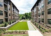 Thumbnail 4 of 72 - A long, narrow, grassy area separates two rows of apartment buildings.
