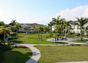 Thumbnail 10 of 33 - A pathway in a park with palm trees and houses in the background at The Crest at Laurel Canyon Apartments, Naples, 34113