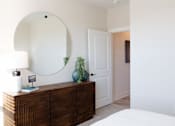 Thumbnail 21 of 66 - A bedroom with a round mirror above a wooden dresser.at Riverside Apartments, Chattanooga