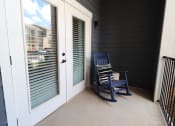 Thumbnail 32 of 60 - a rocking chair on a porch next to a door at The Crest at South Point Apartments, McDonough, GA