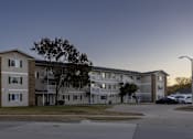 Thumbnail 2 of 11 - an apartment building on a street corner at dusk