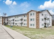 Thumbnail 1 of 11 - Apartment building with a parking lot in front.
