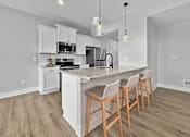 Thumbnail 8 of 12 - A kitchen with a white island and wooden chairs.