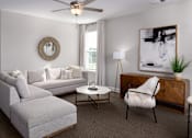 Thumbnail 38 of 44 - A living room with a grey couch, a white coffee table, a white chair, a wooden cabinet, and a painting on the wall.
