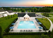 Thumbnail 24 of 44 - A large swimming pool surrounded by lawn chairs and umbrellas with a house in the background.