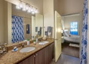 Thumbnail 33 of 38 - Bathroom with double vanity sinks pictured. Cabinets are dark brown with granite counter tops. Bathroom entry located within one of the bedroom at The Bartram Apartments in Gainesville, FL 32608